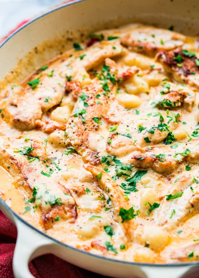 a braiser full of chicken and gnocchi in a creamy sauce garnished with parsley