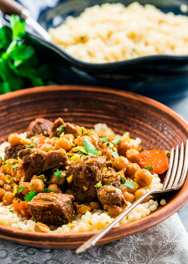 a bowl of lamb and chickpea stew over couscous with a fork