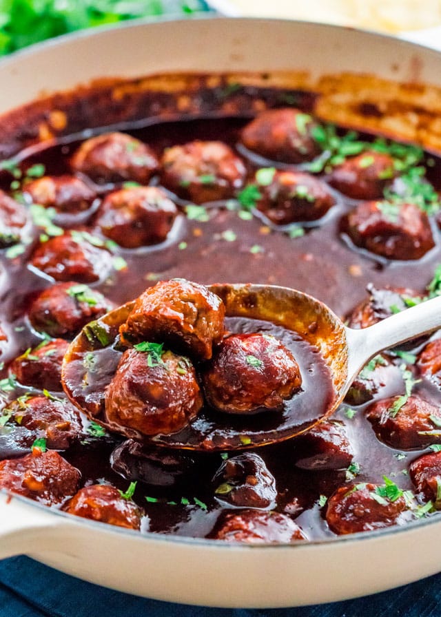 a spoon scooping 3 meatballs out of a braiser filled with sauce and meatballs