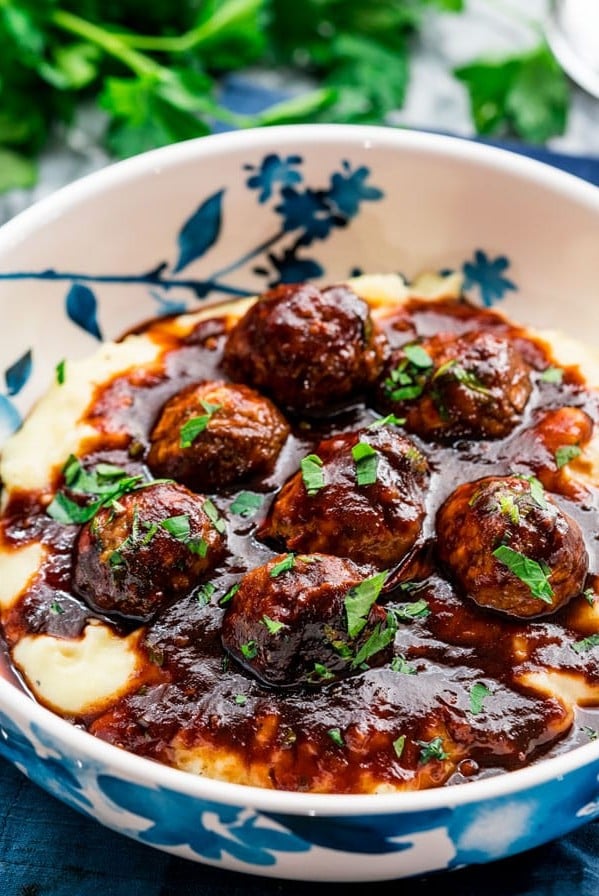 side view shot of a bowl of mashed potatoes topped with stout meatballs with beer and bbq sauce