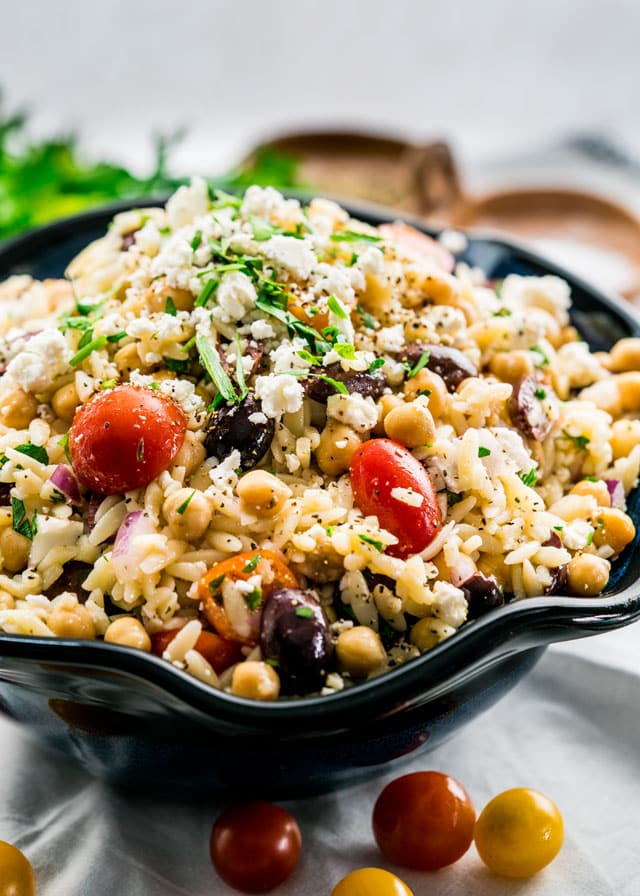 a large bowl full of orzo salad with feta, olives, tomatoes, chickpeas, and onion.