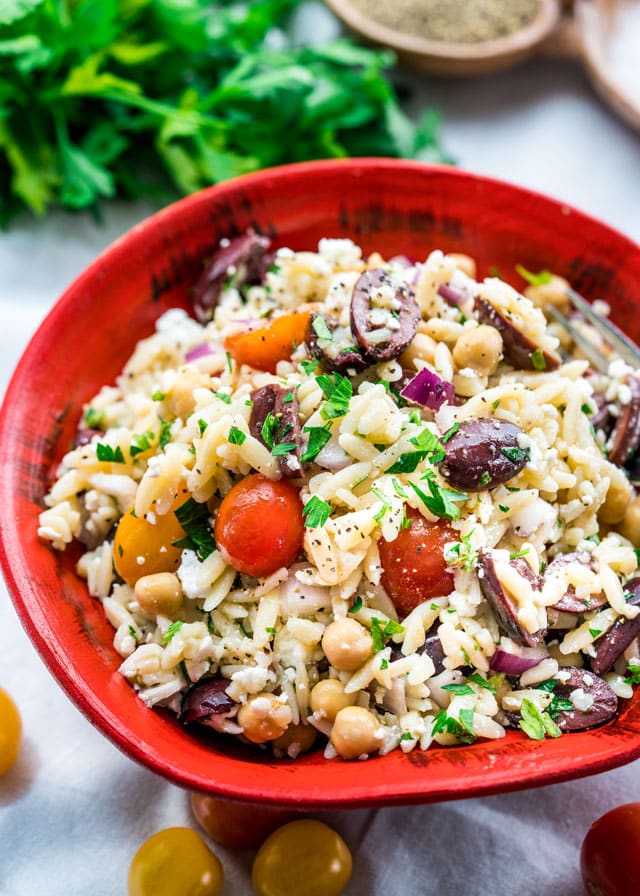 a bowl full of orzo salad with tomatoes, olives, chickpeas, feta, and onion.