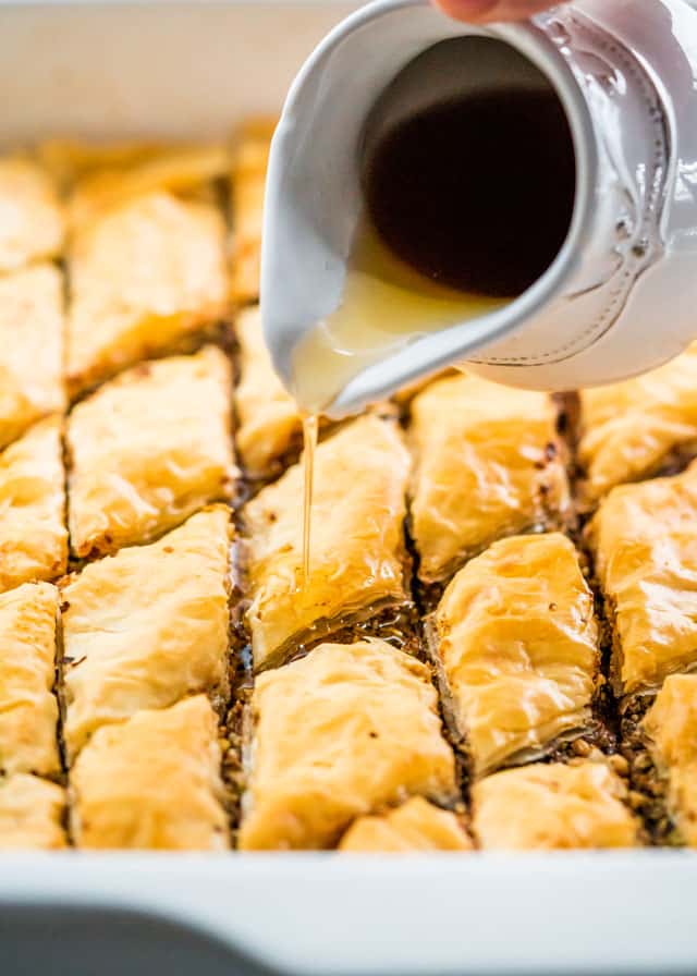 drizzling honey syrup over a pan full of baklava