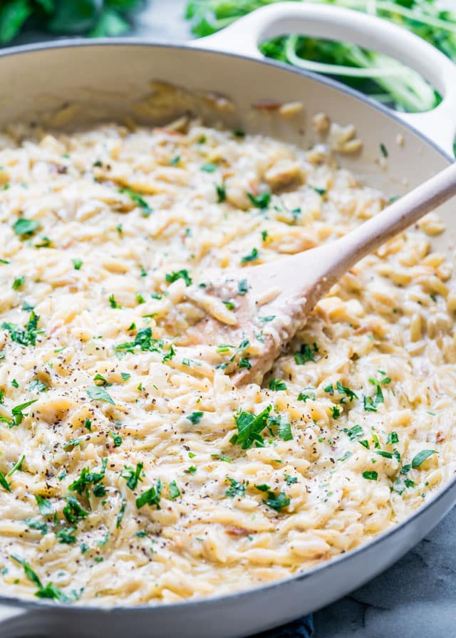 creamy parmesan orzo in a braiser with pepper, parsley, and a wooden spoon