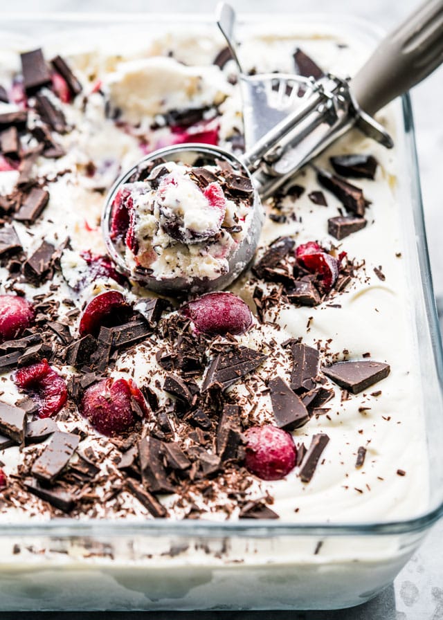 an ice cream scoop in a pan full of ice cream topped with cherries and chocolate