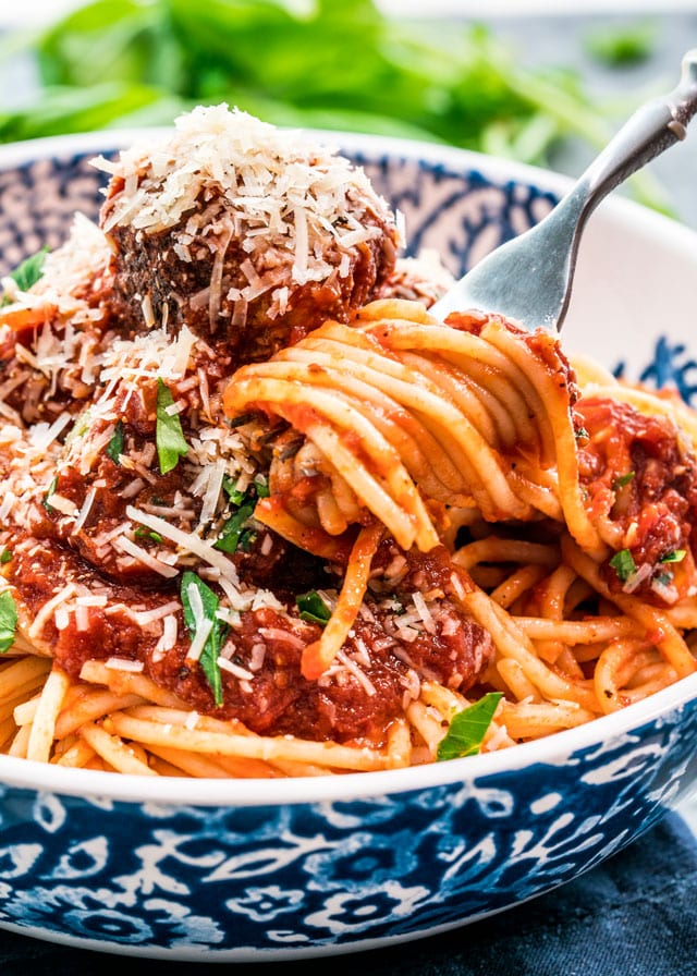 a fork twirling spaghetti from a bowl with meatballs and parmesan