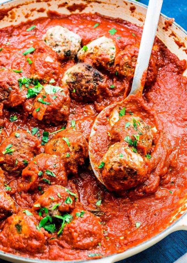 a spoon scooping 2 meatballs out of a large braiser
