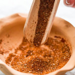 side view close up shot of a handle holding a wooden scoop pouring fajita seasoning into a small dish