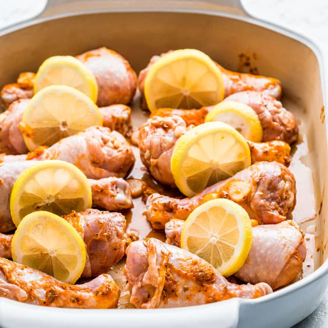 chicken legs seasoned in a casserole dish ready to bake with lemon slices