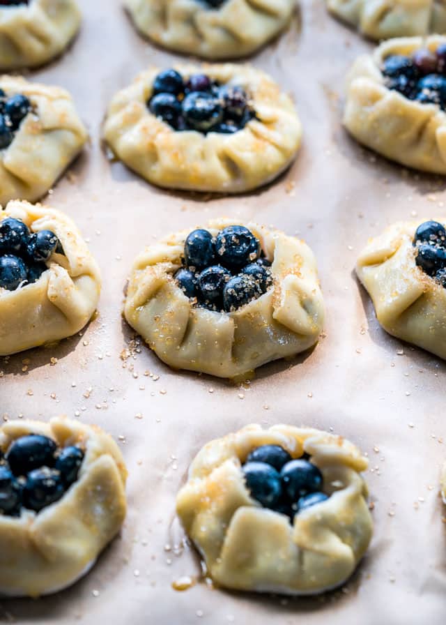 uncooked mini blueberry galettes on a baking sheet topped with sugar
