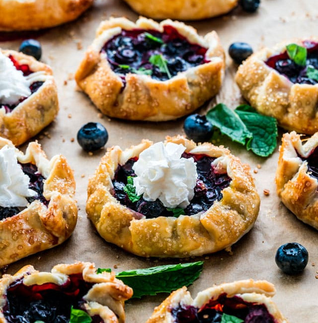 side view shot of mini blueberry galettes, 3 are topped with a dollop of whipped cream