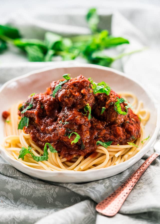 meatballs covered in sauce over a plate of spaghetti garnished with basil