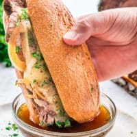side view shot of a hand dipping the french dip into a small bowl of au jus