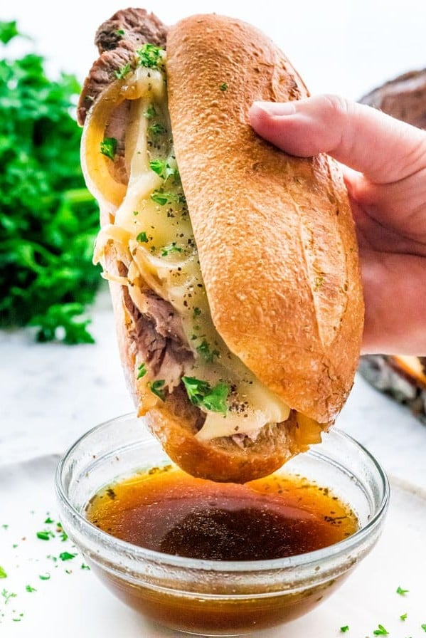 side view shot of a hand about to dip the sandwich in the au jus