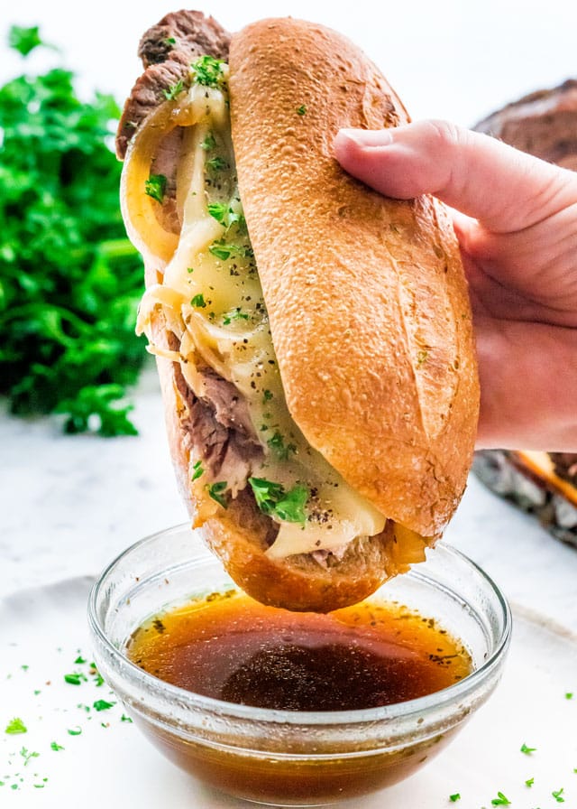 side view shot of a hand about to dip the sandwich in the au jus