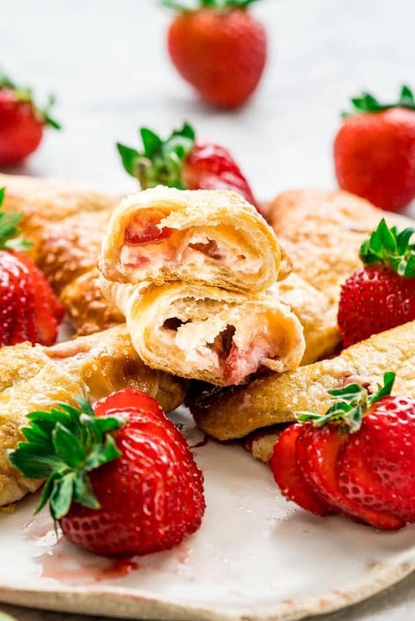 side view shot of strawberry cheesecake crescent rolls on a plate, one ripped in half exposing the center