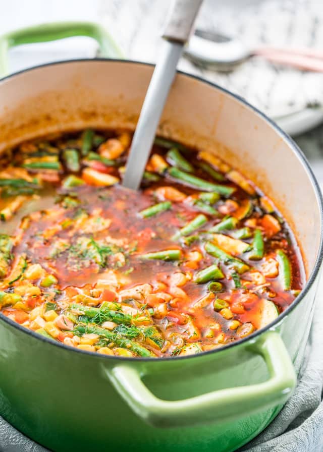 a large pot of soup filled with vegetables and chicken with a ladle