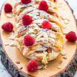 side view shot of peaches and cream strudel topped with sliced almonds and raspberries on a wooden plank