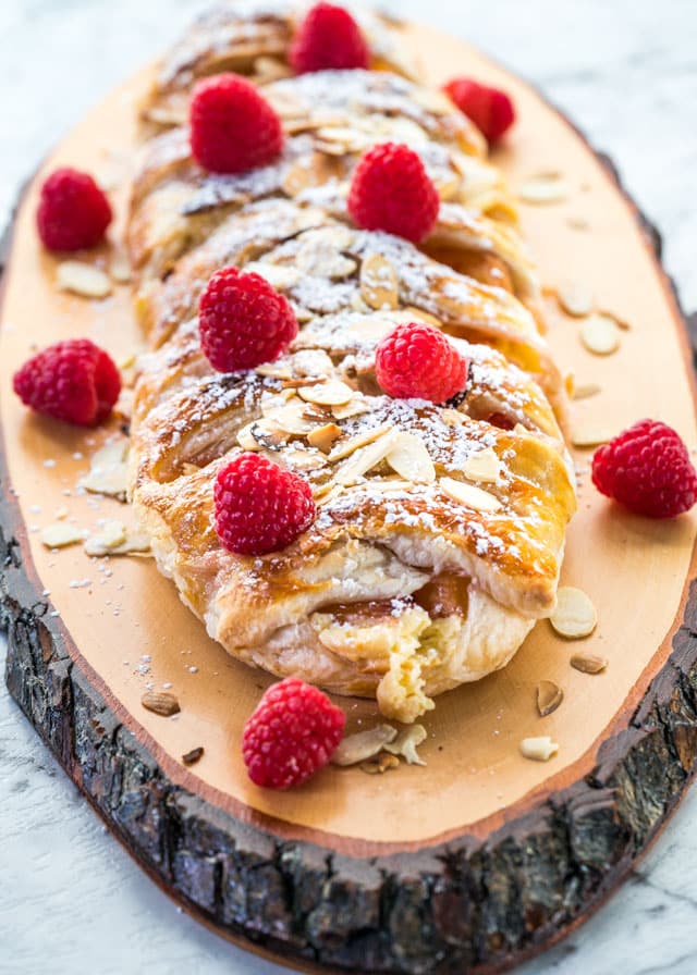 strudel topped with raspberries and almonds on a plank of wood