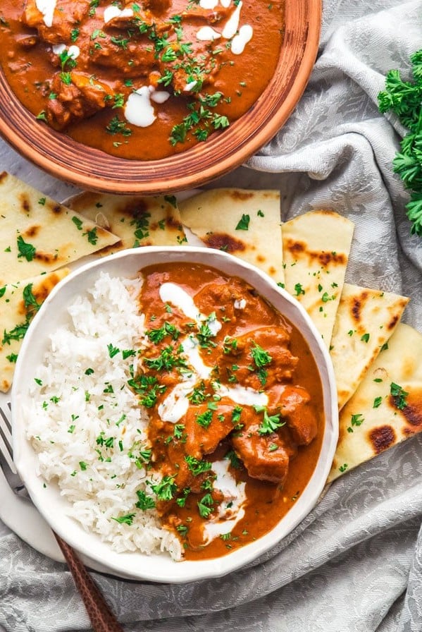 overhead shot of instant pot butter chicken with a side of rice surrounded by pita bread