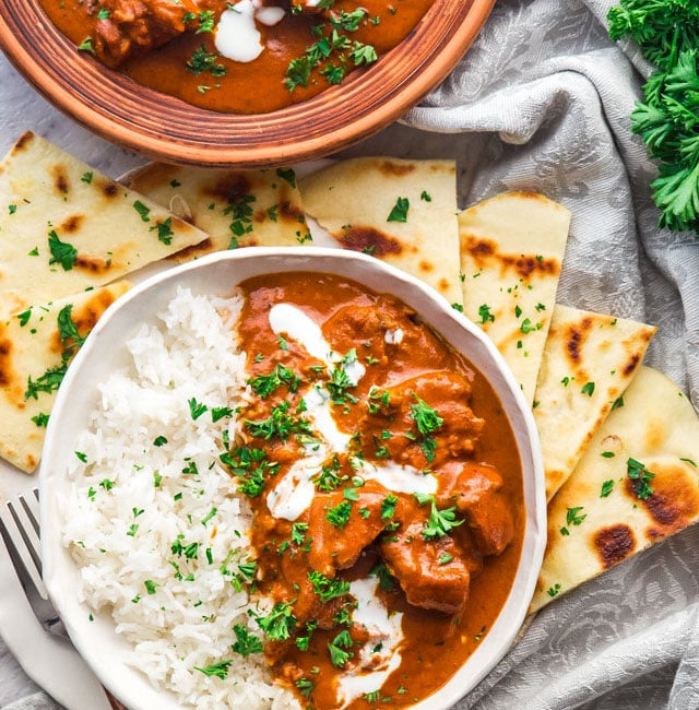 overhead shot of instant pot butter chicken with a side of rice surrounded by pita bread