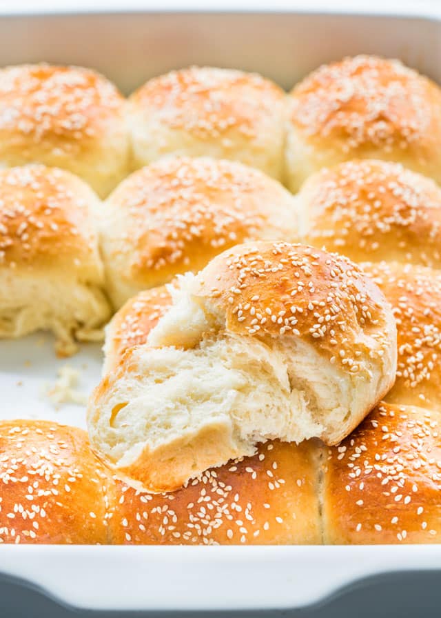 freshly baked buttermilk dinner rolls with sesame seeds in a baking dish with one roll broken in half