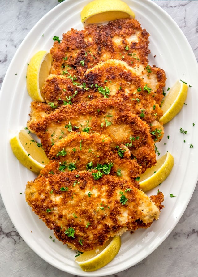 Overhead of a platter of Chicken Schnitzel with lemon wedges and parsley