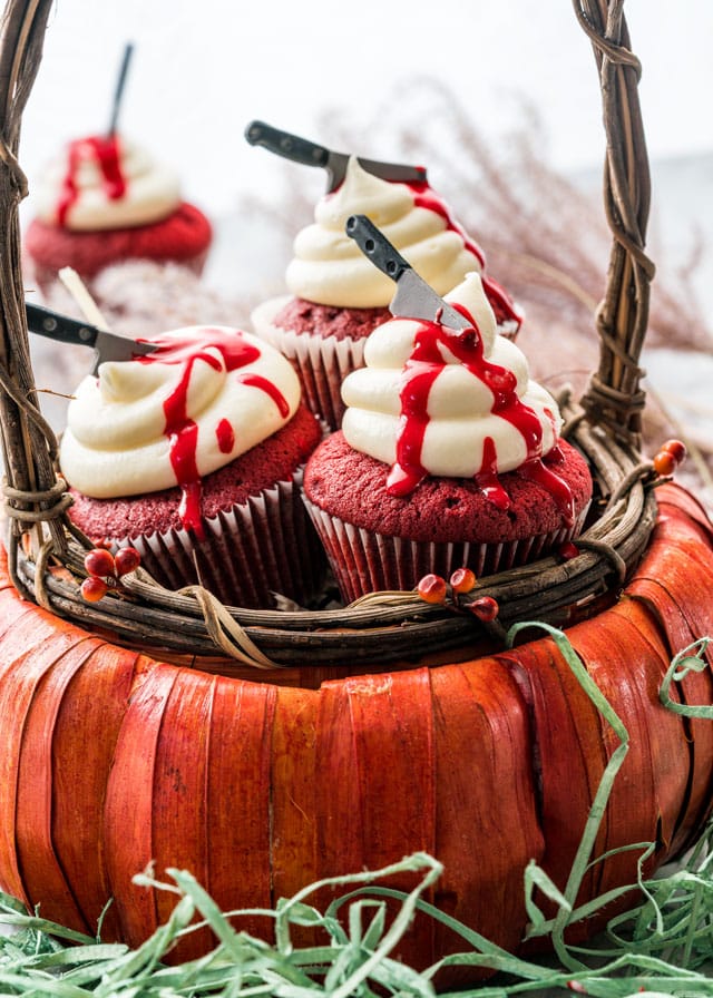 red velvet cupcakes in a pumpkin shaped basket with icing and candy knives