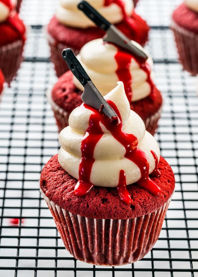 red velvet cupcakes on a cooling rack with icing and a candy knife