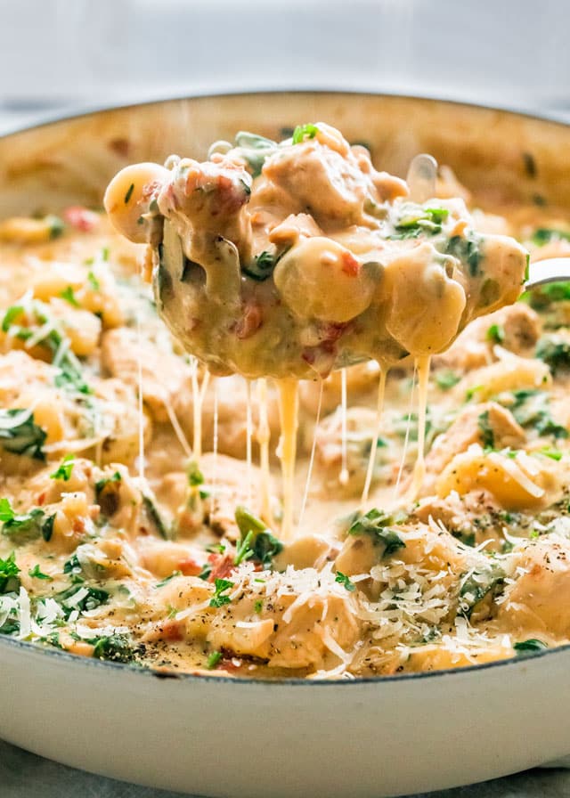A spoon holding up one pot chicken florentine gnocchi with melted cheese in a skillet