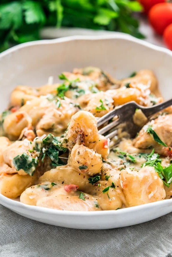 side view shot of a fork taking a bite of chicken florentine gnocchi from a bowl