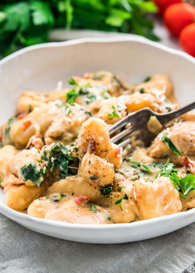 A white plate of Chicken Florentine Gnocchi with a fork scooping out a bite
