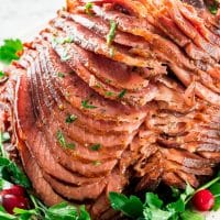 side view shot of the honey mustard glazed ham, sliced on a serving platter garnished with fresh parsley and cranberries