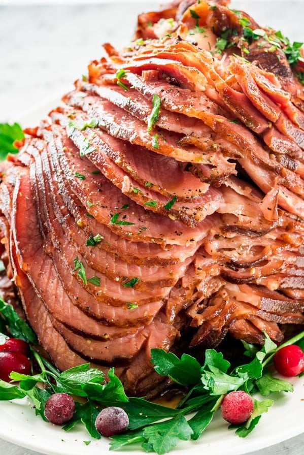 side view shot of the honey mustard glazed ham, sliced on a serving platter garnished with fresh parsley and cranberries