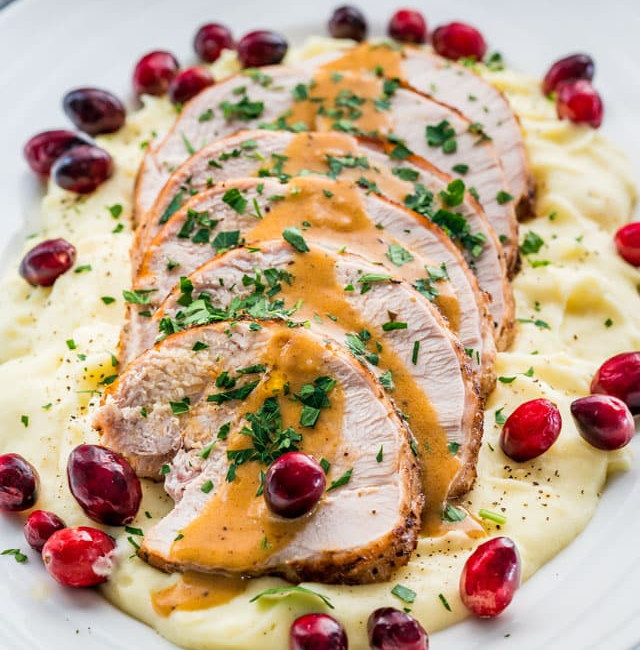 side view shot of sliced turkey breast drizzled with gravy atop a pile of mashed potatoes on a plate garnished with fresh cranberries