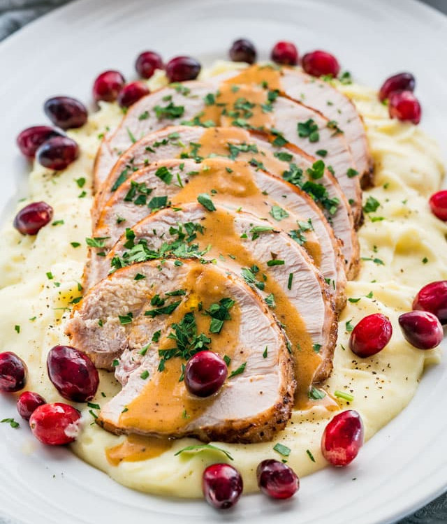 side view shot of sliced turkey breast drizzled with gravy atop a pile of mashed potatoes on a plate garnished with fresh cranberries