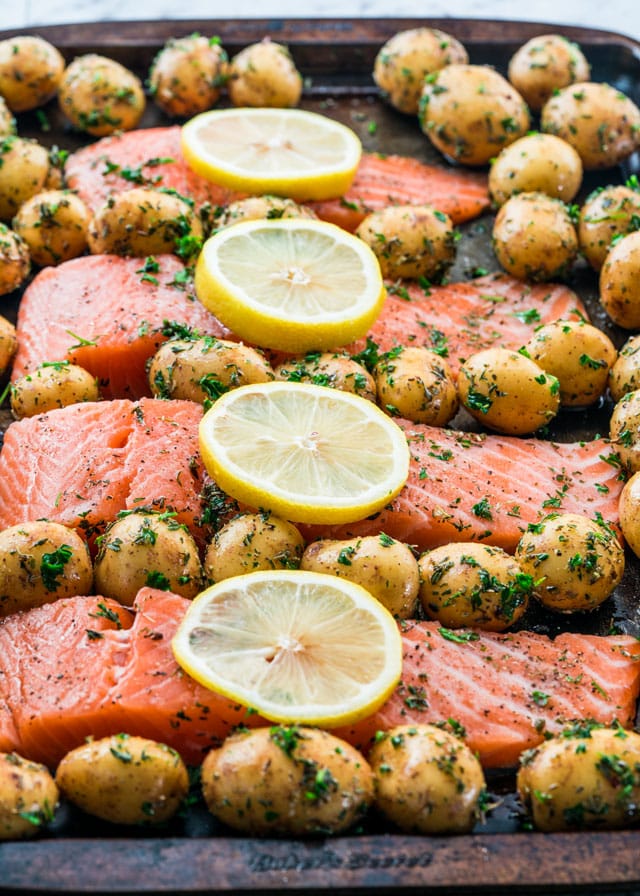 Salmon filets topped with lemon slices and surrounded by baby potatoes on a pan waiting to go in the oven