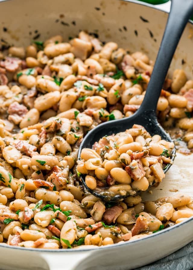 Serving spoon scooping out some White Beans with Bacon and Herbs from the pan