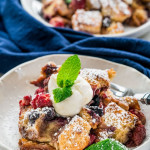 side view shot of a bowl full of berry brioche bread pudding topped with a dollop of whipped cream and a sprig of mint