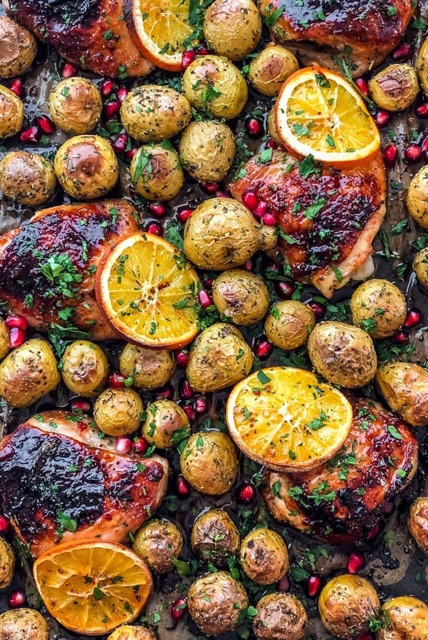 overhead shot of roasted honey orange chicken and potatoes topped with orange slices, pomegranate seeds and chopped parsley