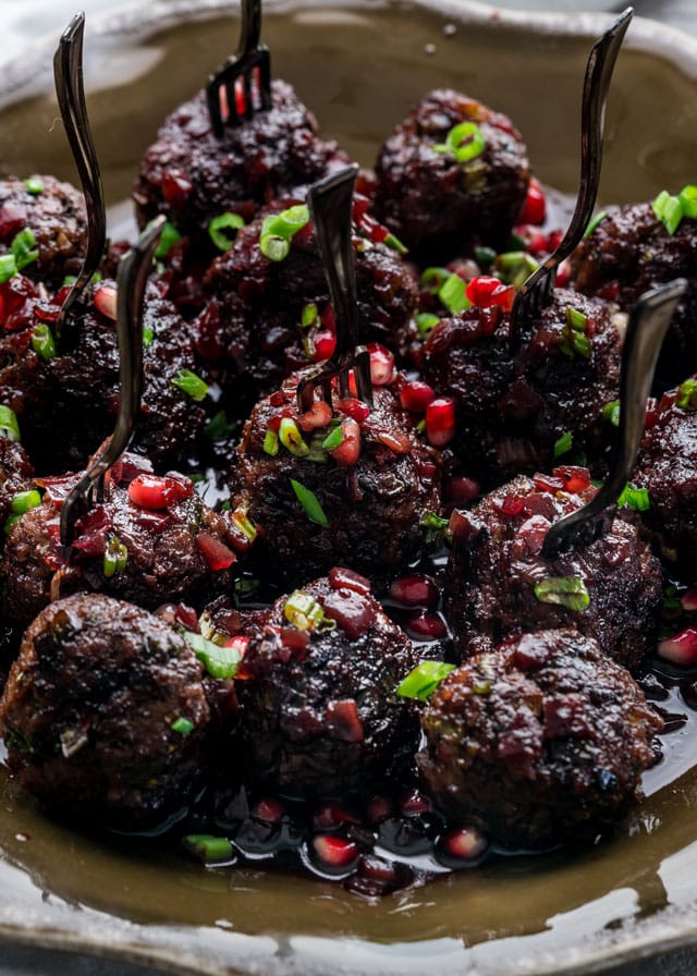 close up shot of a plate full of pomegranate cocktail meatballs with cocktail forks stuck in them