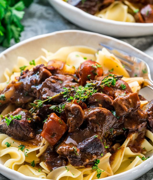 side view shot of a bowl of noodles topped with beef bourguignon