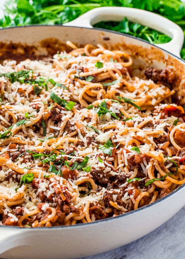 spaghetti bolognese in a large skillet with grated parmesan cheese and parsley