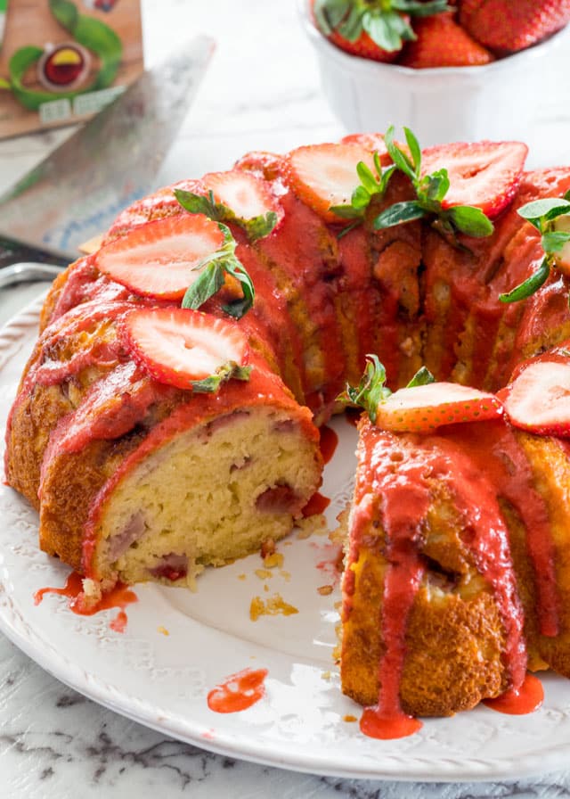 Strawberry Lemon Bundt Cake on a cake platter drizzled with strawberry coulis and topped with fresh strawberries