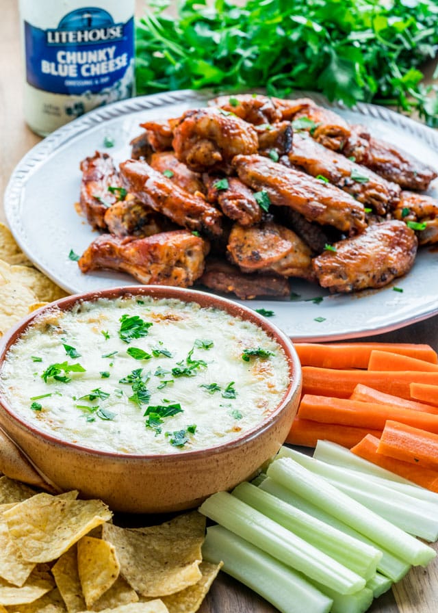 Blue cheese dip with tortilla chips, celery and carrots alongside a plate of hot wings