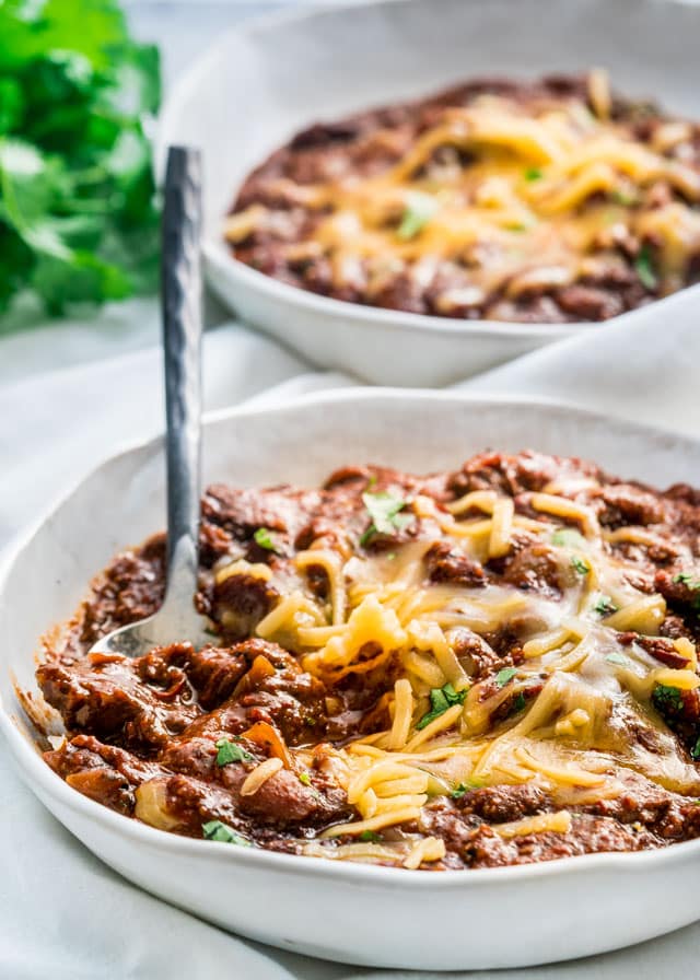 two plates loaded with beef chili and topped with cheese
