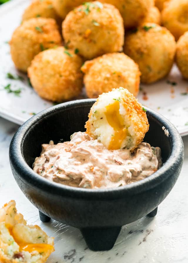 half a potato croquette in a bowl with sour cream dip and a plate of potato croquettes in the background