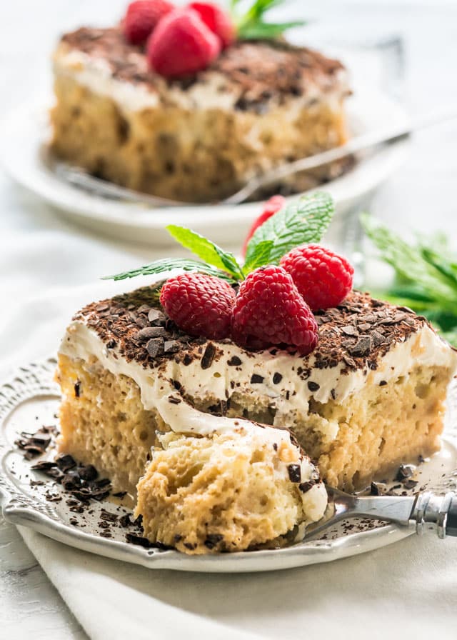 Tiramisu Tres Leches Cake slice on a white plate with raspberries and chocolate on top