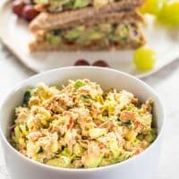 side view shot of a bowl full of avocado tuna salad with a tuna salad sandwich in the background