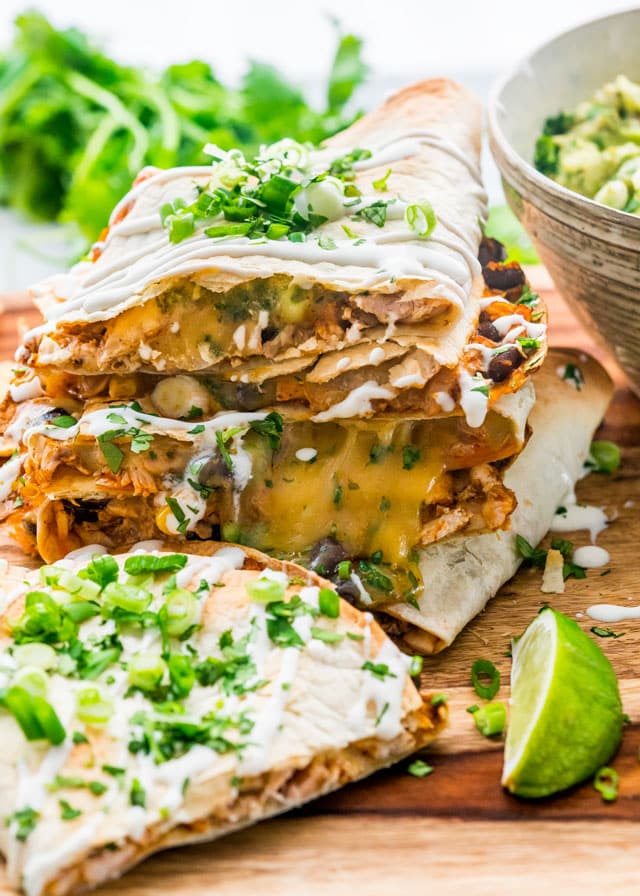 chicken enchilada quesadillas stacked on a cutting board garnished with sour cream, cilantro and green onions